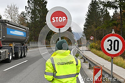 Road supervisor from behind with stop sign - road block due to a construction site in Salzkammergut, Austria, Europe Editorial Stock Photo